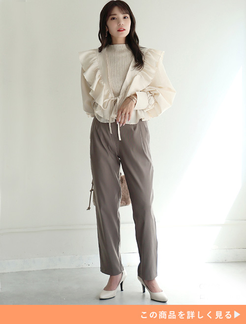 アイボリー色のフリルブラウス×モカ色のテーパードパンツを着る女性