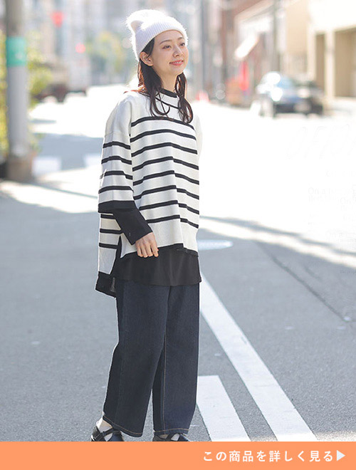 黒インナーにボーダー柄ニットプルオーバーを重ねて着て、濃デニムパンツを履く女性