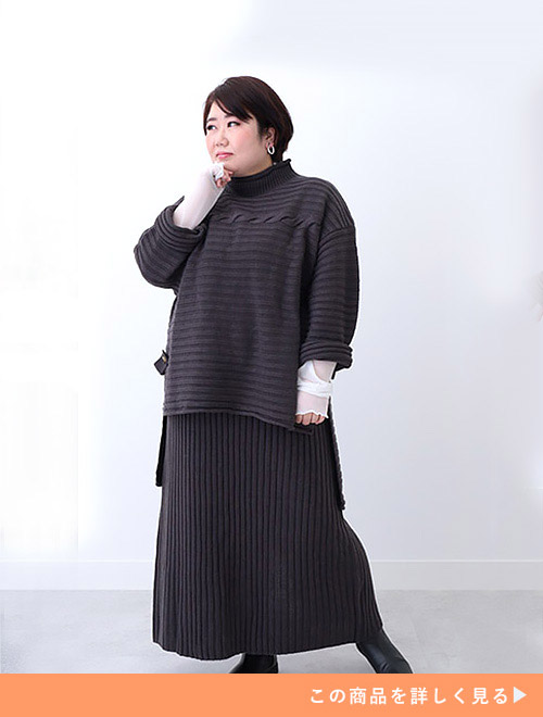 モカチャコール色のニットアップを着て、袖からシアートップスをのぞかせる女性