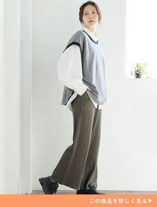 白シャツにモノトーンのベストを重ね着して、カーキ色のワイドパンツを履く女性
