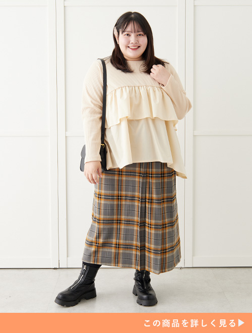 白のティアードトップスにチェックのスカートを穿く女性