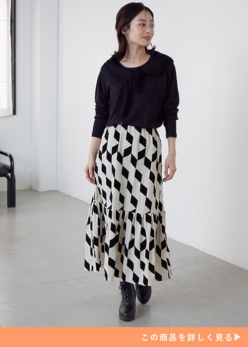 黒のシンプルトップスをモノトーンの幾何学柄ロングスカートにトップスインして着る女性