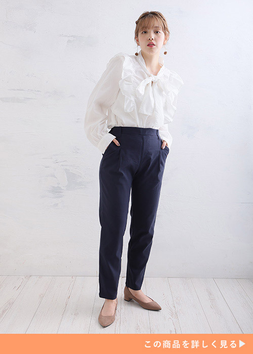 白のリボン体ブラウスを着て、ネイビーのテーパードパンツを履く女性