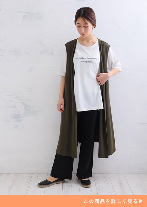 白トップス×黒パンツにカーキの半袖ロングジレを羽織る女性。