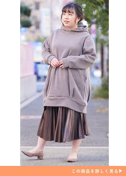 サーモンピンクのパーカにブラウンのプリーツスカートを履いた女性