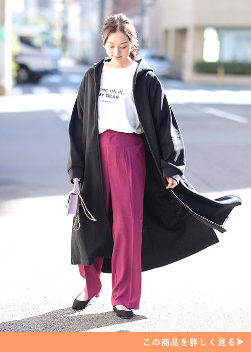 ピンクのカラーパンツに白T、黒のロング丈パーカを着た女性