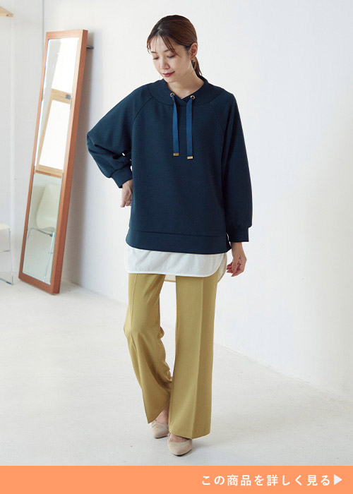 くすみイエローのパンツに紺のパーカを着た女性