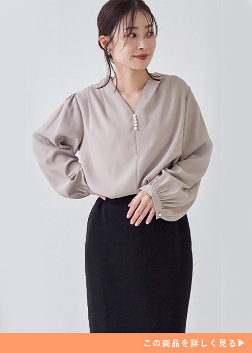 Vネックのパールボタン付きブラウスを着て、黒ボトムを履く女性