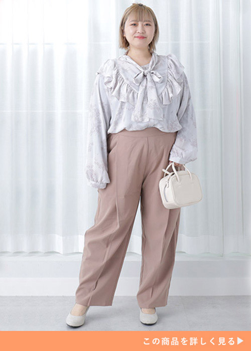 淡い花柄のフリルブラウスを着て、グレージュのストレートパンツを履く女性