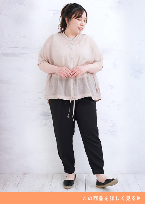 透け感のあるグレージュのフレンチスリーブトップスを着て、黒パンツを履く女性