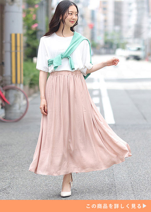 白Tシャツ×ピンクオレンジのフレアースカートを履き、黄緑のトップスを肩に掛けたる女性