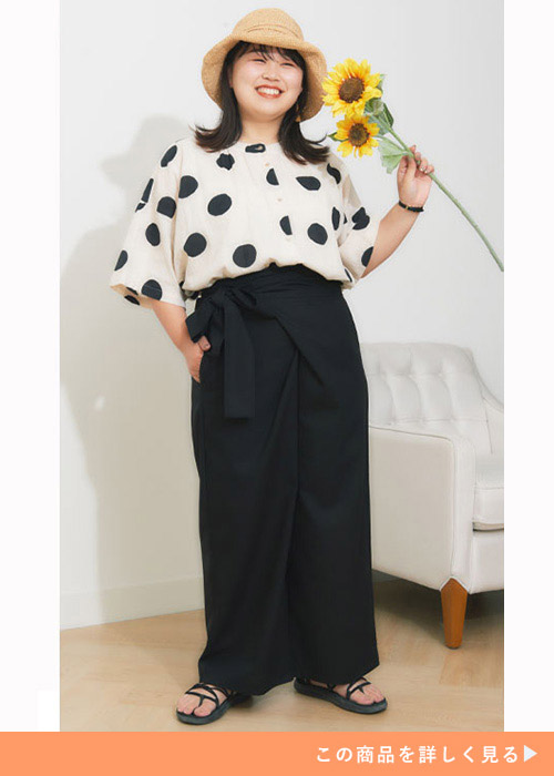 白地に黒のドット柄トップスを黒の巻きワイドパンツにトップスインして着る女性