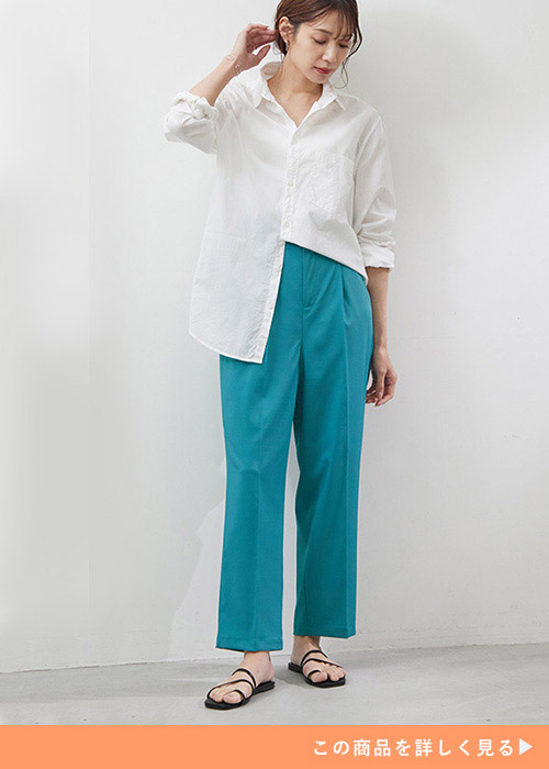 ピーコックグリーンのパンツに白シャツの片裾だけインして着る女性