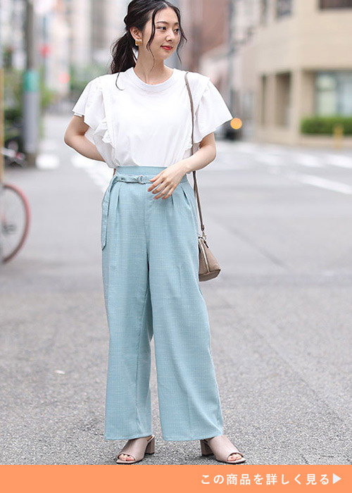 淡いブルーのワイドパンツにフリル付き白トップスを着た女性