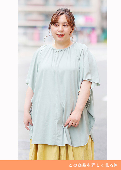 黄色ボトムにセージグリーンのポンチョ風トップスを着て、右に視線を送る女性