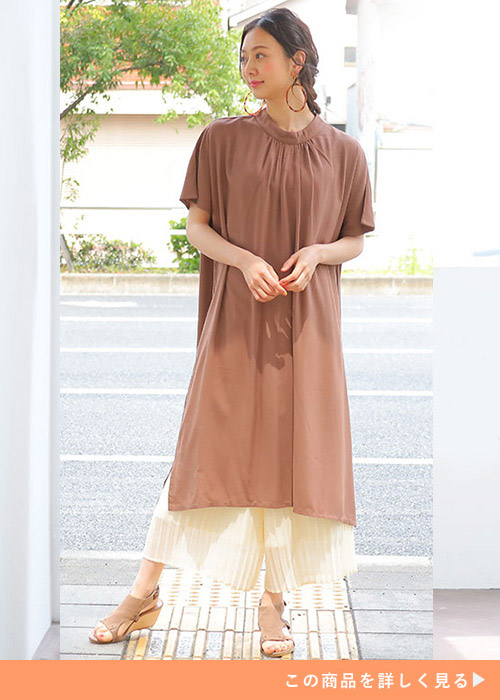 ブラウンのギャザーワンピースに白のワイドパンツを合わせて、右側を見る女性