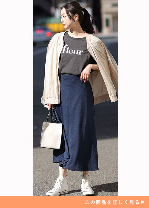 紺のタイトスカートにロゴTを合わせてベージュのジャケットを羽織った女性