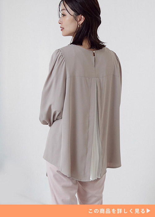 グレージュのブラウスに薄いピンクのパンツを合わせて、背中を向けた女性