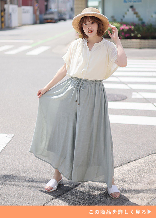 ライトグリーンのワイドパンツにシアー素材のシャツを合わせた女性