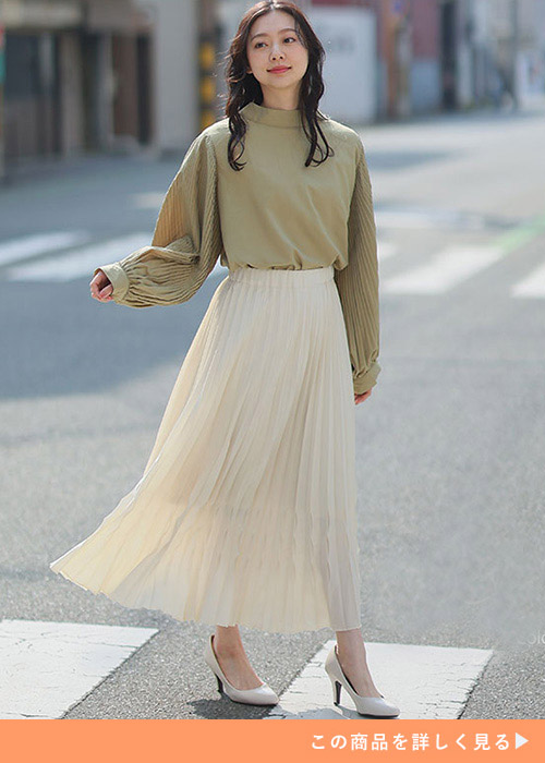 白のプリーツスカートに袖プリーツのトップスをインする女性