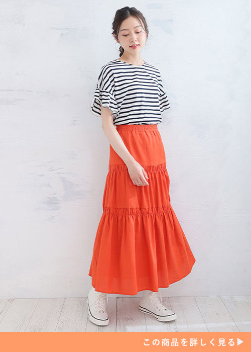 ボーダートップスとオレンジのボリュームスカートのコーデに白いスニーカーを履く女性