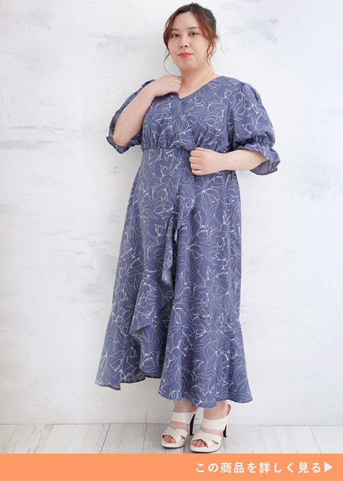 カシュクールとフリルのアシメトリーワンピースに白いサンダルを履く女性