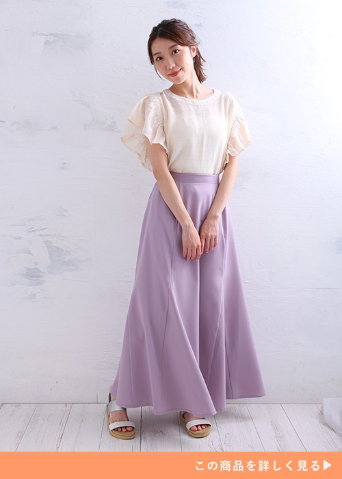 白いトップスと薄いパープルのスカートのコーデに、ヌーディーなサンダルを履く女性