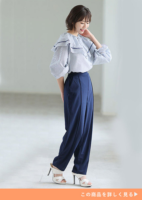 ブルーのブラウスとネイビーのテーパードパンツのコーデに白いサンダルを履く女性