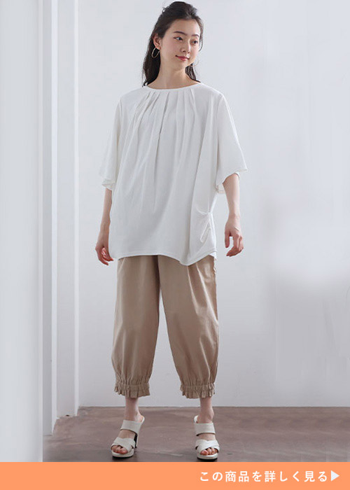 オフホワイトのトップスとベージュのパンツのコーデに白いサンダルを履く女性