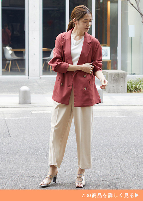 コーラルピンクのジャケットにホワイトのトップスとパンツを合わせる女性