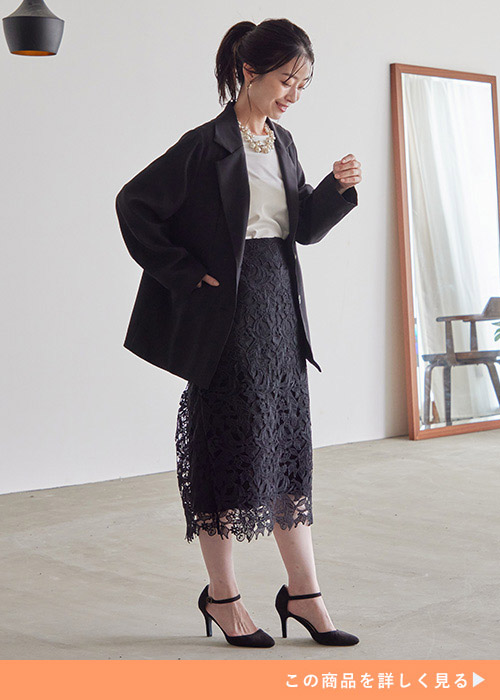 黒のジャケットと黒のレーススカートのコーデに黒いパンプスを履く女性。