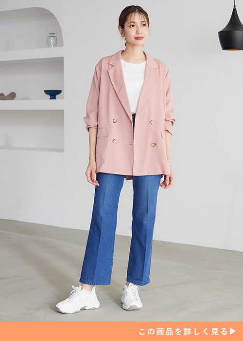 ピンクのダブルボタンジャケットと白トップスとデニムパンツのコーデの女性