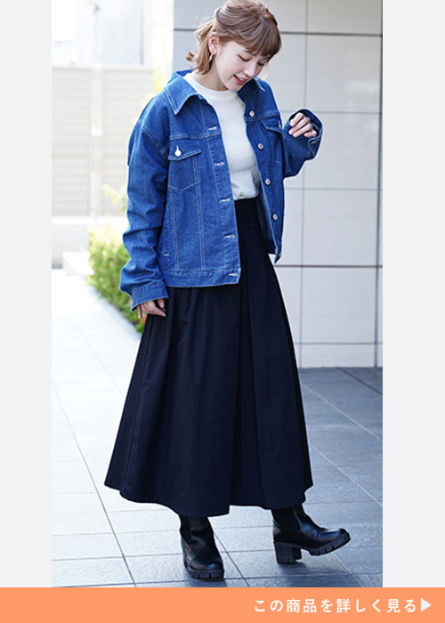 デニムジャケットとネイビーのスカートのコーデに黒いブーツを履く女性