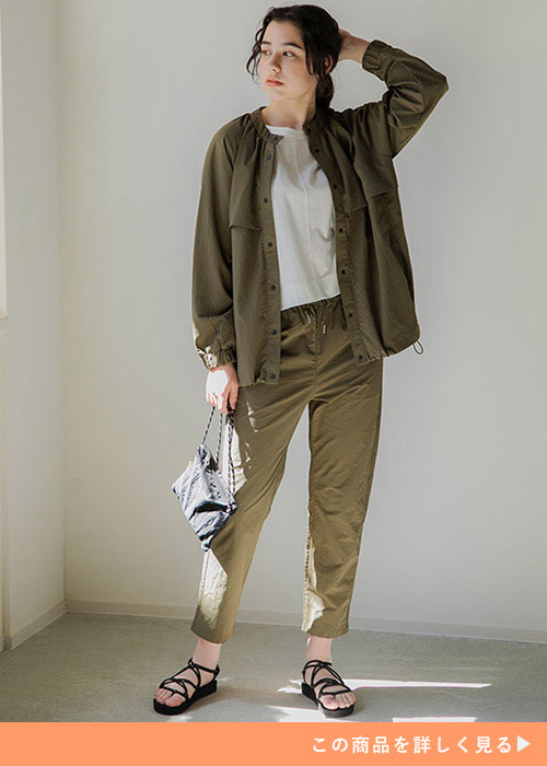 カーキのミリタリージャケットとパンツのコーデに黒いサンダルとクラッチを合わせる女性。