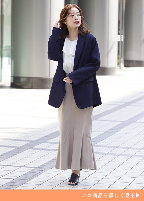 ネイビーのテーラードジャケットにフリルブラウスとマーメイドスカートを合わせる女性