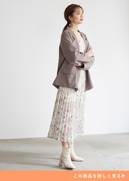 モカのテーラードジャケットとプリーツワンピースのコーデに白いブーツを履く女性