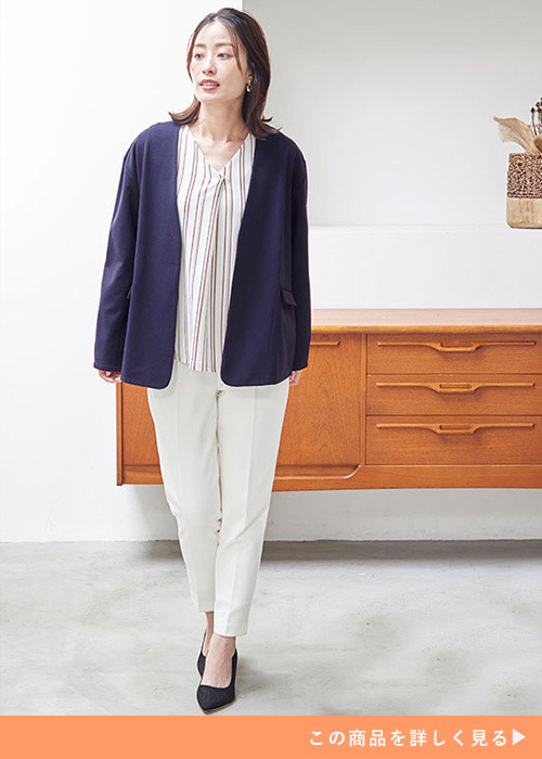 ネイビーのジャケットとストライプブラウスとホワイトパンツのコーデに黒いパンプスを履く女性