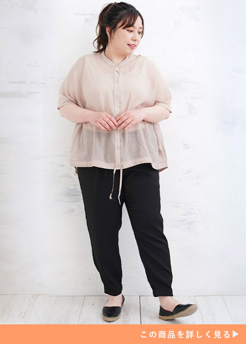 グレージュのシアートップスを着て、黒のパンツとフラットシューズを履く女性