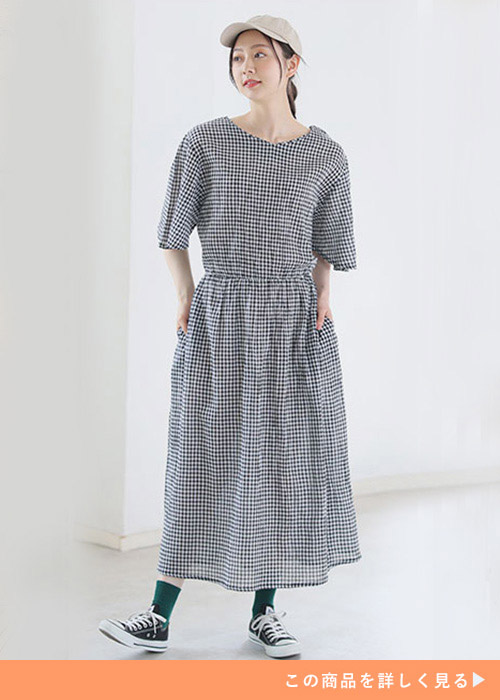 ギンガムチェックのワンピースを着て、ベージュのキャップを被り、スニーカーを履く女性