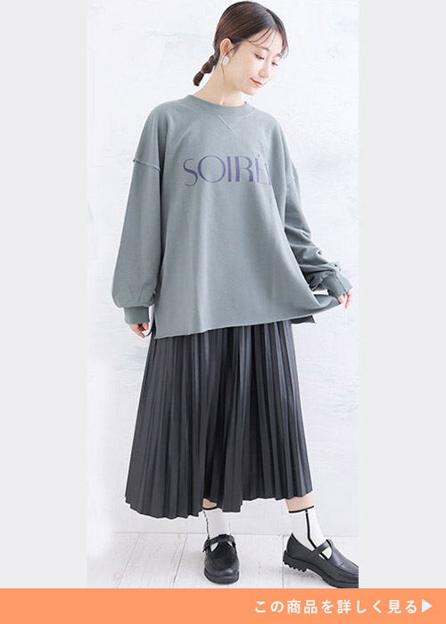 グリーンのロゴスウェットを着て、黒のプリーツスカートを履く女性