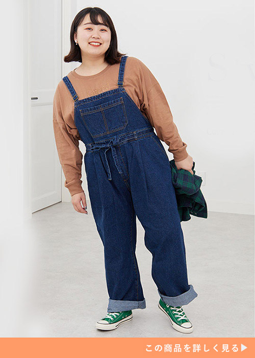 茶のロンTにネイビーのサロペットを着て、緑のスニーカーを履く女性。