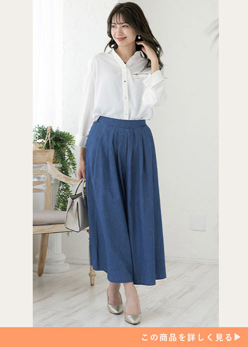 デニムロングスカートと白シャツのコーデにパンプスを履く女性