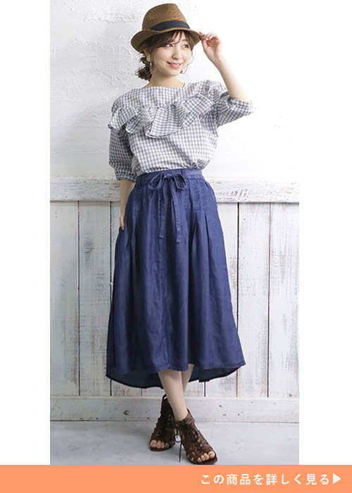 テールヘムのデニムスカートとチェックのブラウスにグラディエーターサンダルを履く女性