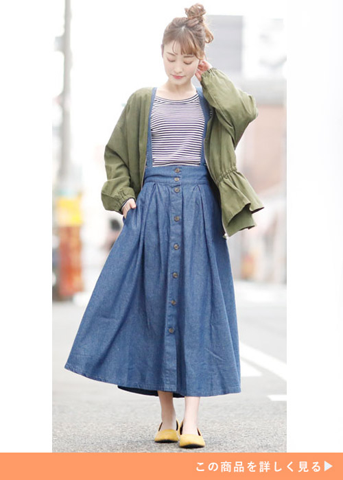 サスペンダー付きデニムスカートとボーダートップスのコーデにカーキのジャケットを羽織る女性