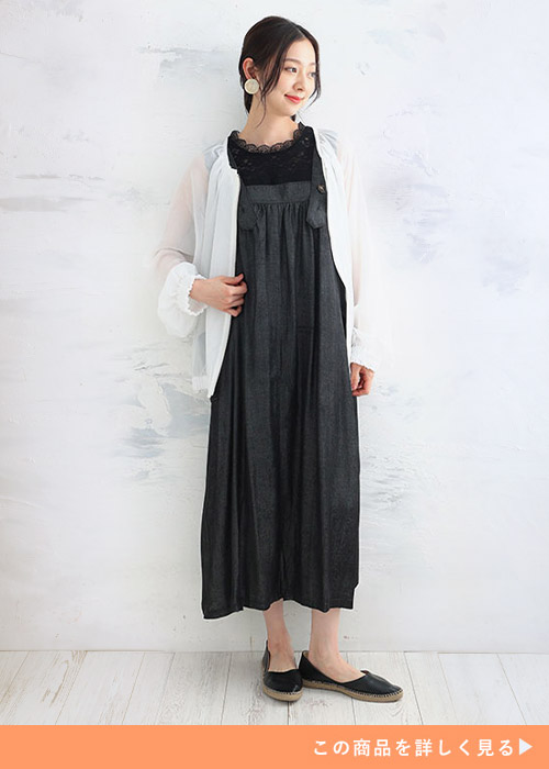 デニムワンピースに白いジャケットを羽織り、黒いフラットシューズを履く女性