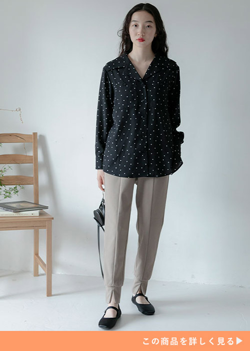 黒地に白のドット柄ブラウスを着て、モカベージュのジョガーパンツを履く女性