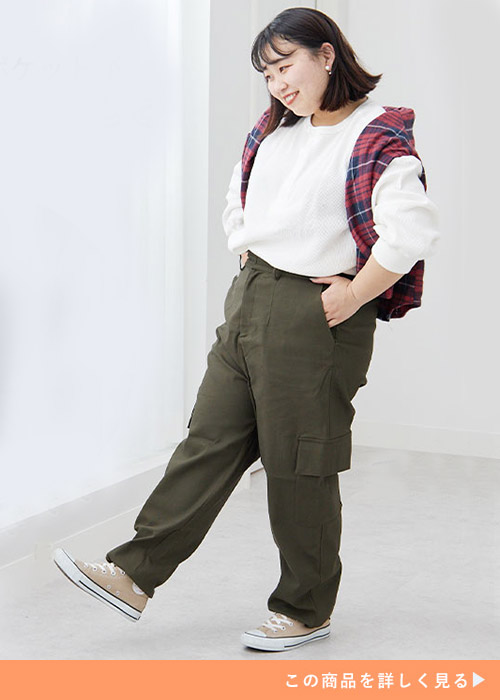 白トップスを着て、カーキのカーゴパンツを履き、赤のチェック柄シャツを肩掛けする女性