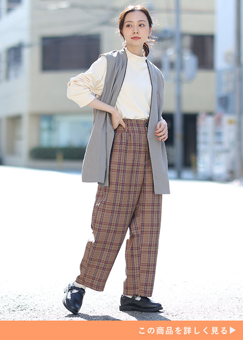 アイボリーのトップス×ブラウン系のチェク柄テーパードパンツに、グレーのジレを羽織る女性