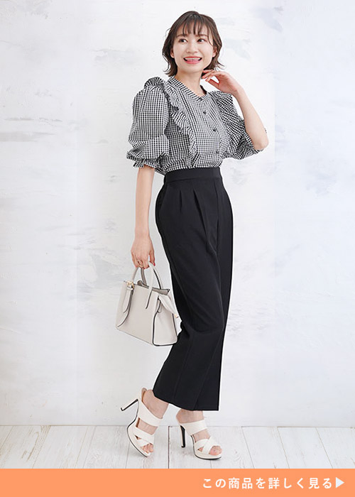 ギンガムチェック柄の肩フリルブラウスを着て、黒のテーパードパンツを履く女性