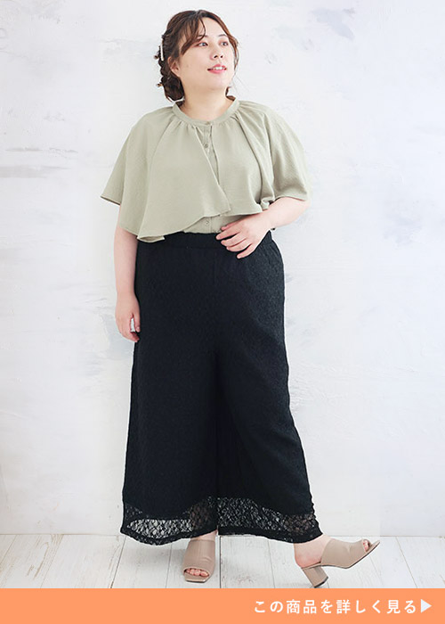 くすみグリーンのブラウスを着て、黒のレース生地ワイドパンツを履く女性